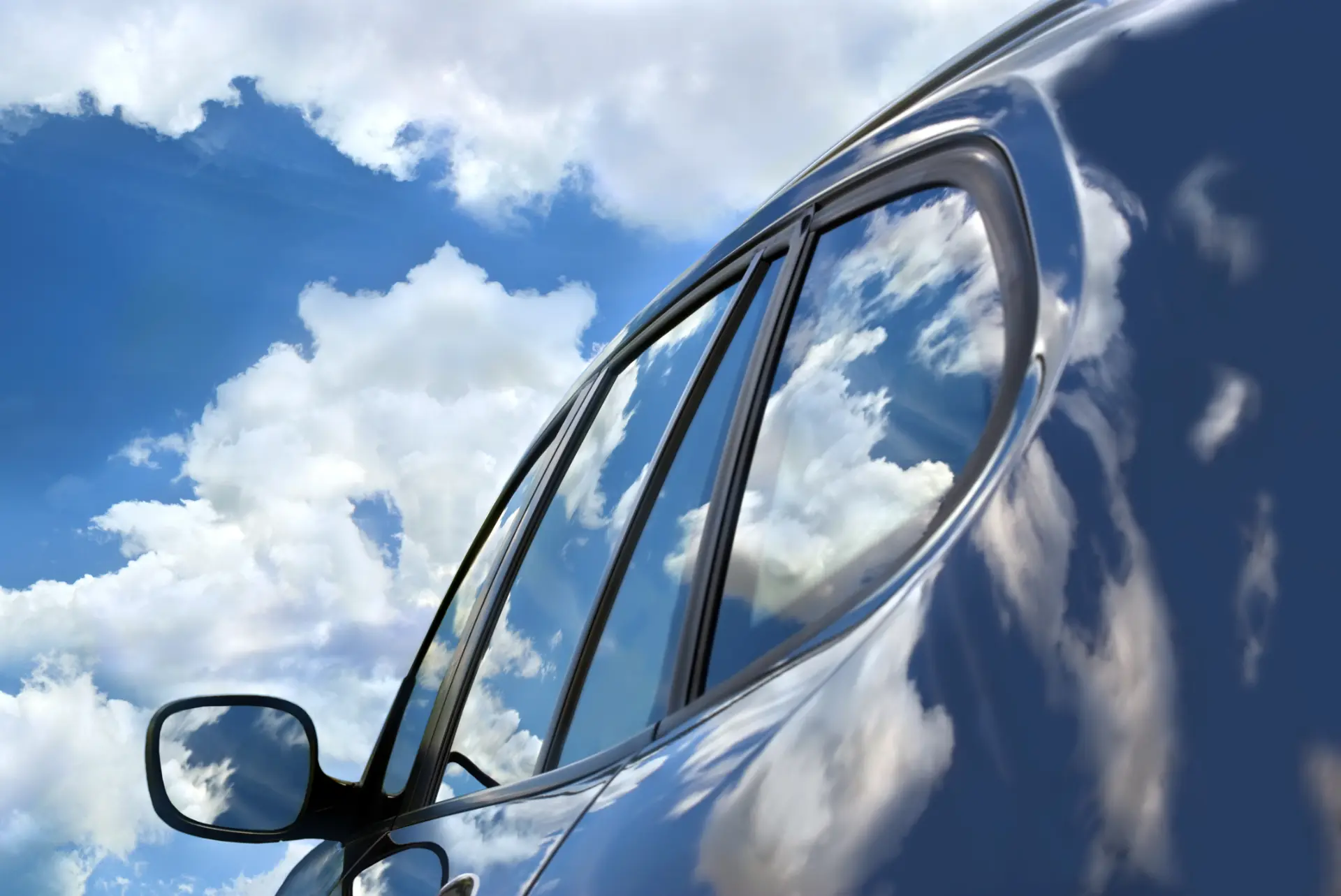 Car side window reflecting clouds and blue sky