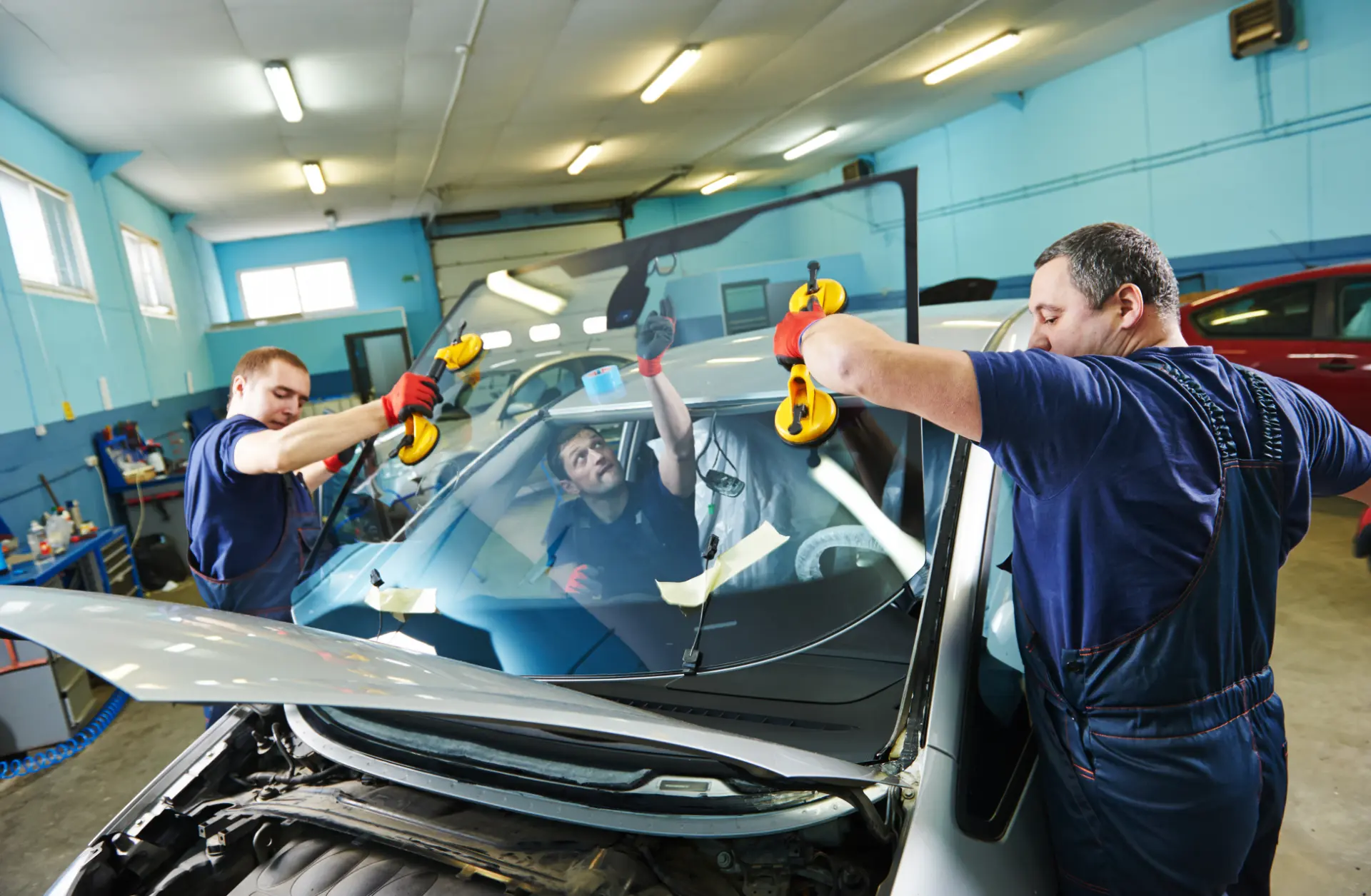 Three technicians replacing a windscreen at an auto glass shop